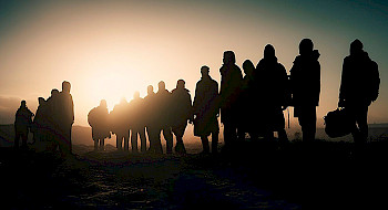 Siluetas de migrantes caminando al atardecer.