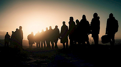 Siluetas de migrantes caminando al atardecer.