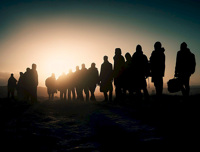 Siluetas de migrantes caminando al atardecer.