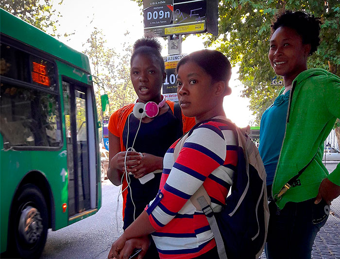 Tres jóvenes inmigrantes se encuentran en un paradero de buses en Santiago.