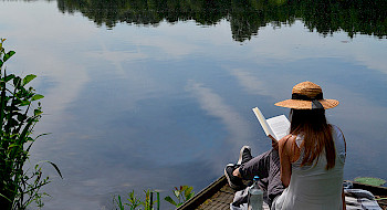 Mujer leyendo en un muelle con agua y vegetación de fondo