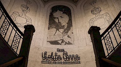 Vista del hall de entrada a la Casa Violeta Parra, con un mural y detalles en hierro forjado en la baranda.