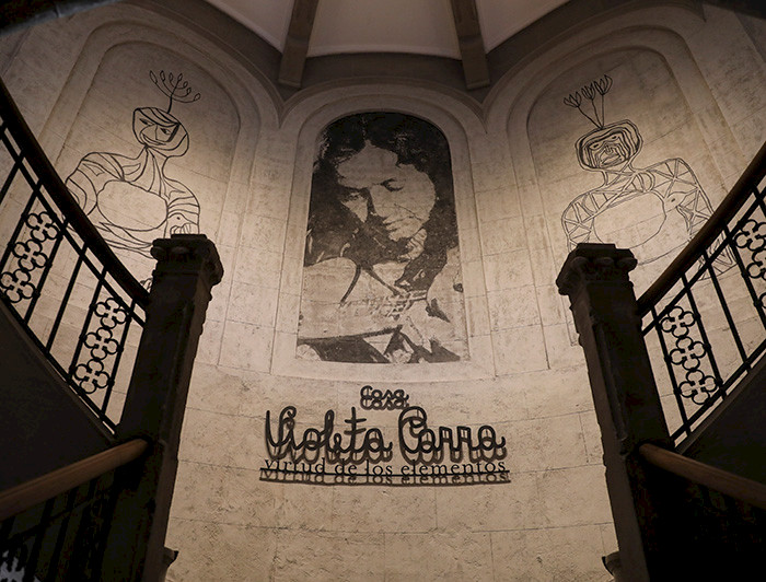 Vista del hall de entrada a la Casa Violeta Parra, con un mural y detalles en hierro forjado en la baranda.