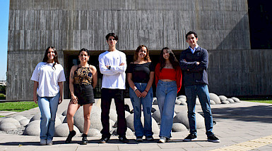 A diverse group of students posing outside a university building, representing unity and collaboration in a vibrant academic setting.