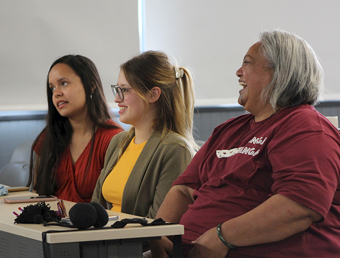 Three women sitting in a classroom, smiling and engaging in discussion.