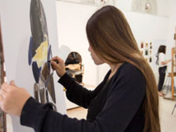 Una mujer pintando sobre un lienzo, en una sala de pintura.
