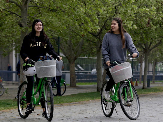 Dos estudiantes arriba de dos bicicletas, en el campus San Joaquín. Fotografía: Banco de Imágenes UC.