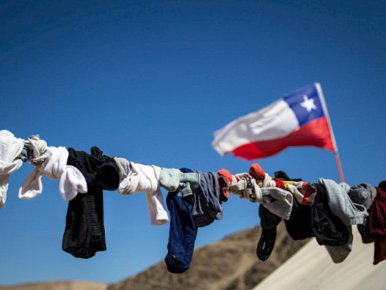 Ropa tendida contra cielo azul y bandera chilena. (Foto: Karina Fuenzalida)